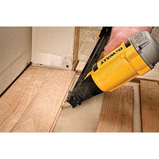 DEWALT nailer being used to secure wooden flooring near a wall during installation.