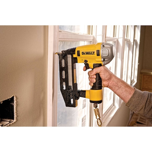 A DEWALT pneumatic nailer is used to fasten trim on a window frame during construction or renovation work.