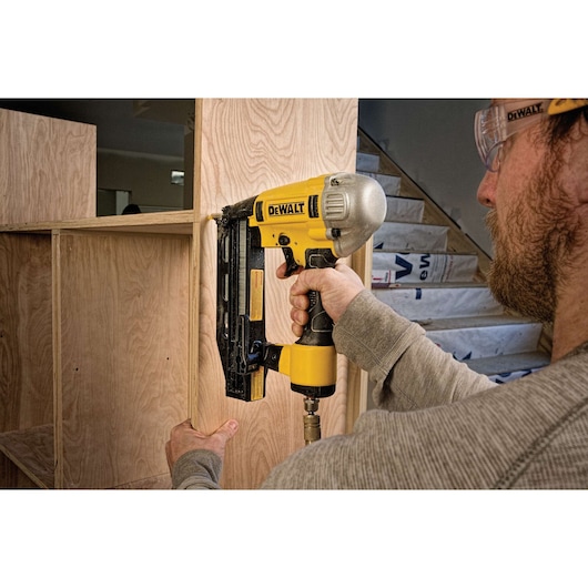 Person using a DEWALT nail gun to assemble wooden shelving during construction.