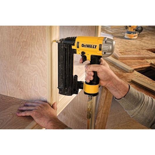 Hand using DEWALT nail gun to attach wooden trim to cabinet during woodworking project.