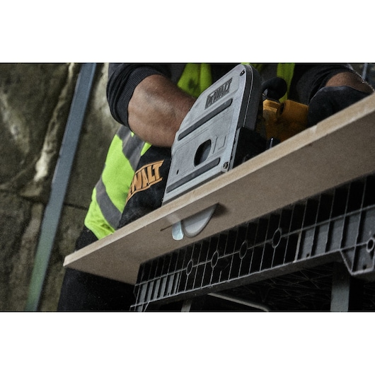 Person using a DEWALT saw to cut wood on a workbench. Close-up view, focus on tool and wood.