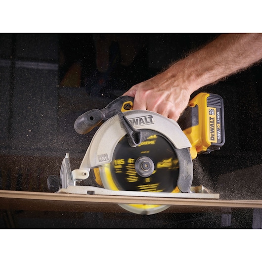 A DEWALT cordless circular saw cutting wood, held by a person, with sawdust flying.