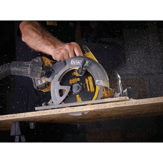 DEWALT circular saw cutting wood, generating sawdust, operator's hand visible in action.