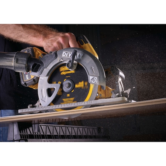Hand holding a DEWALT circular saw, cutting through a wooden board with visible sawdust.