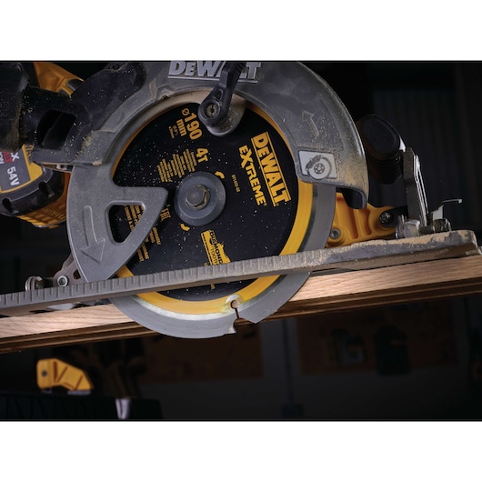 Close-up of a DEWALT circular saw cutting wood, showing the blade and guard in action.