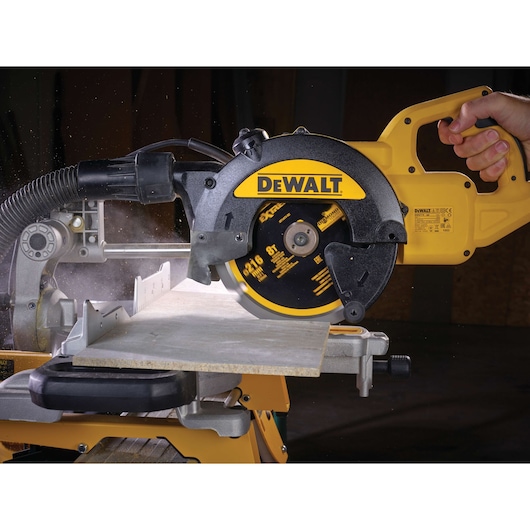 DEWALT circular saw cutting a piece of wood, held by a hand, showing dust and action.