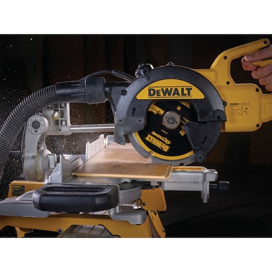 DEWALT circular saw cutting wood, close-up view with dust extraction hose attached, blade in action.