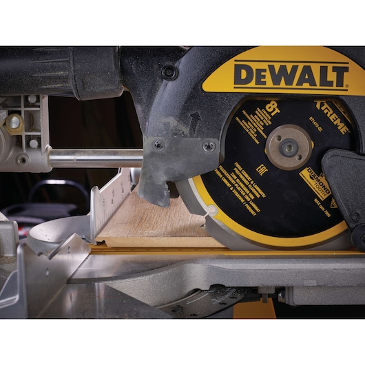 Close-up of a DEWALT circular saw cutting wood, showing blade and guide rail.