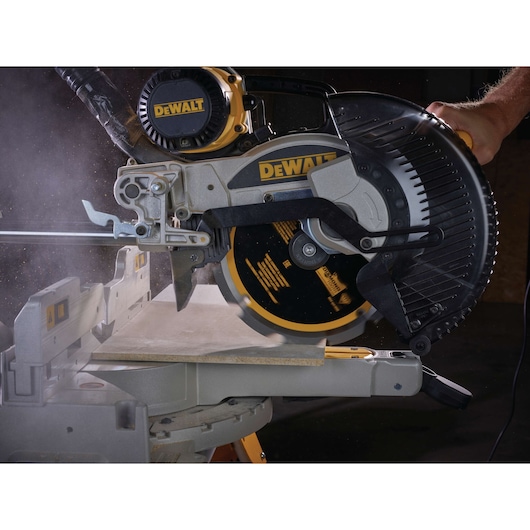A DEWALT miter saw cutting a board, with visible dust and motion during operation.
