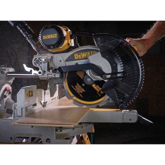 DEWALT miter saw cutting wooden plank, close-up view, dust particles visible during operation.