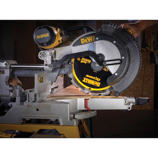DEWALT circular saw cutting wood, close-up of blade and work area on a miter saw in action in workshop setting.