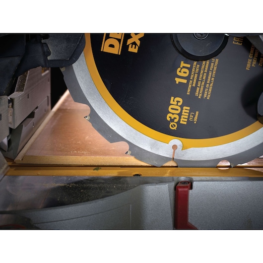 Close-up of a DEWALT circular saw blade cutting through a wooden board with visible dust and measurement marks.