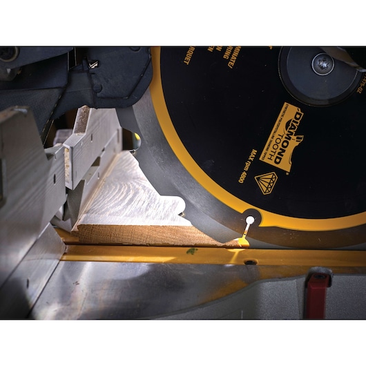 Close-up of a DEWALT DT1475 saw blade cutting a piece of wood on a miter saw.