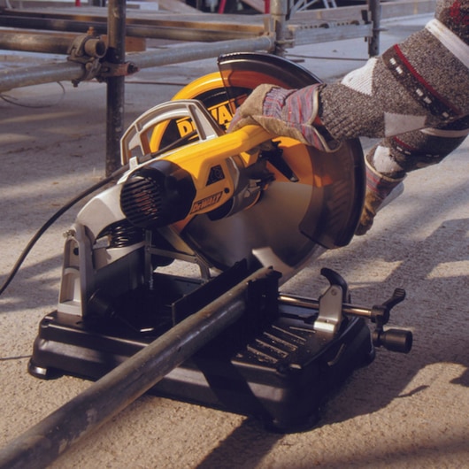 A DEWALT DT1921 circular saw cutting a metal pipe, operated by a gloved hand on a construction site.