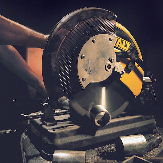 DEWALT metal chop saw cutting a metal pipe in a workshop setting, shown in close-up with protective hand.