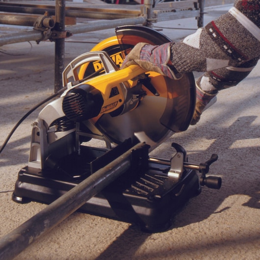 Person uses DEWALT DT1927 power saw to cut metal pipe outdoors. Safety gloves are worn.