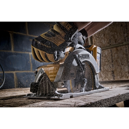 DEWALT circular saw cutting wood, operated by a person wearing safety gloves in a workshop.