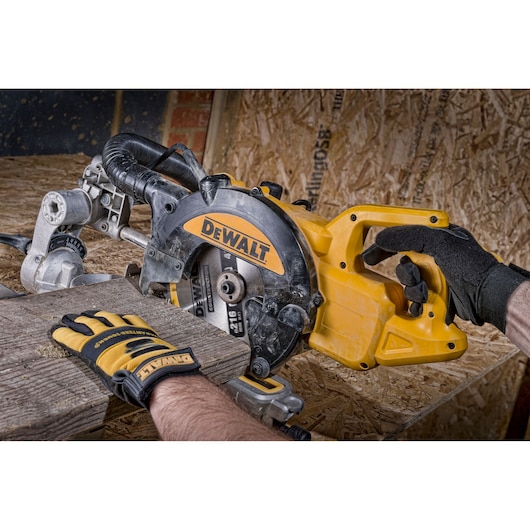 Gloved hands operate a DEWALT circular saw to cut wood on a workbench.