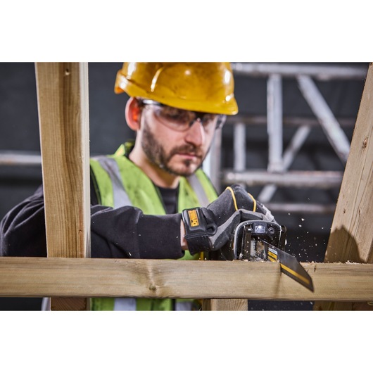 DEWALT glove cutting wood with saw, worker in safety gear, construction site background visible.