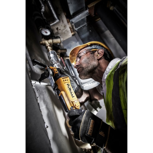 Worker using a DEWALT DT20701 power tool for cutting metal pipes, wearing safety gear in an industrial setting.