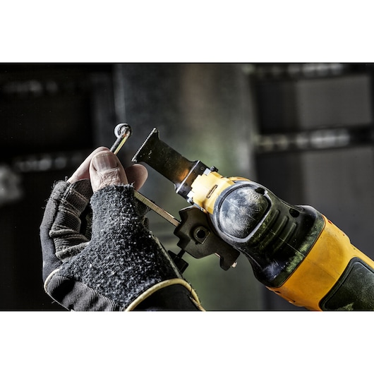 Gloved hand holding DEWALT tool with cutting blade, ready to cut a metal hook.