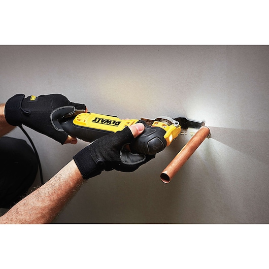 Person uses DEWALT tool to cut wall near copper pipe, wearing black gloves.