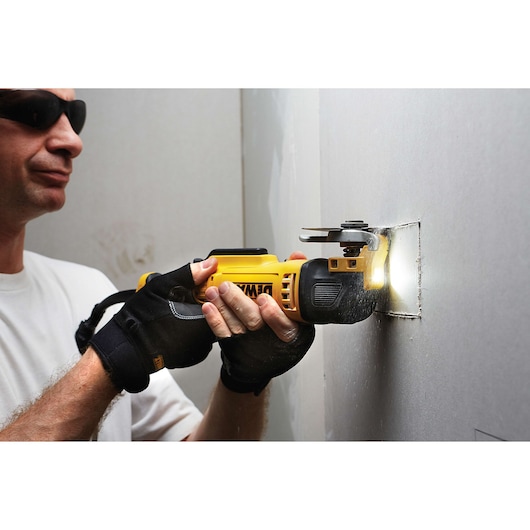 Person uses a DEWALT multitool to cut a square hole in drywall, wearing gloves for safety.