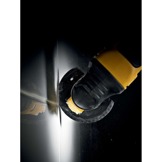 DEWALT tool with blade cutting through metal sheet, close-up view with dark background.