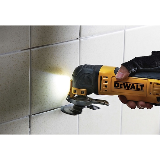 DEWALT multitool being used to cut tiles on a wall, close-up view of hand and tool in action.