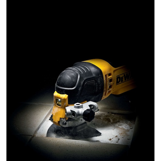 DEWALT multi-tool cutting through tile, creating dust and debris on a tiled surface.