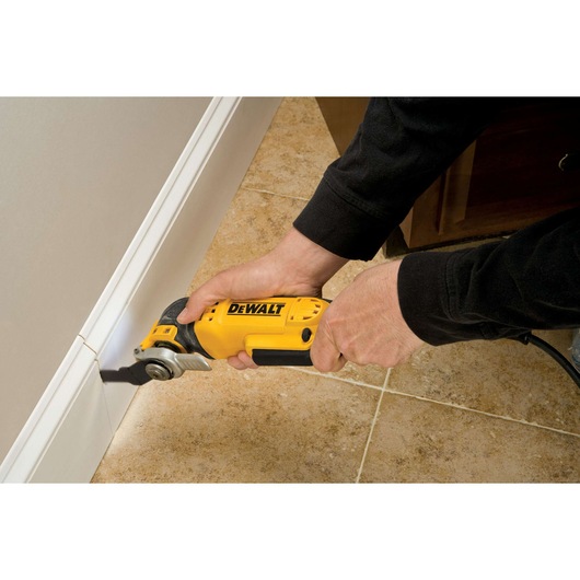 Person using a DEWALT oscillating tool to cut baseboard near tile floor.