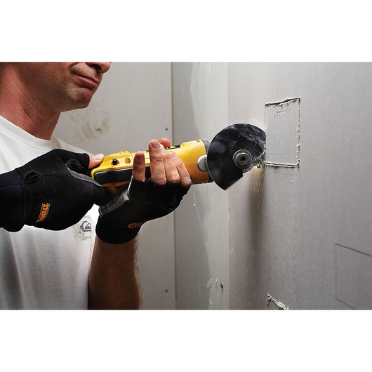 Person uses a DEWALT tool to cut a square in drywall. Wearing black gloves for safety during the job.