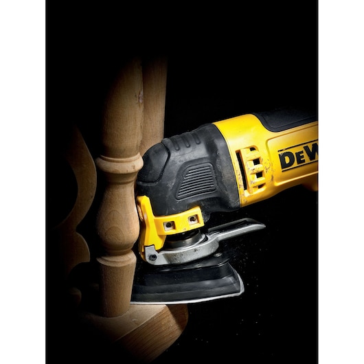 DEWALT sanding tool in use on wooden furniture detail, close-up with partial view of the device and wood surface.