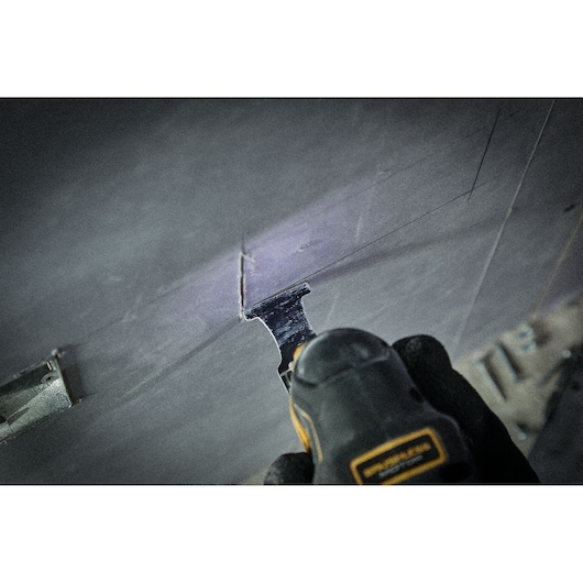 DEWALT oscillating tool cutting a rectangular shape in a wall or panel, operator wearing gloves.