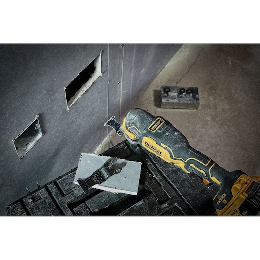 DEWALT multitool cutting drywall for electrical socket installation; tool and cut pieces visible.