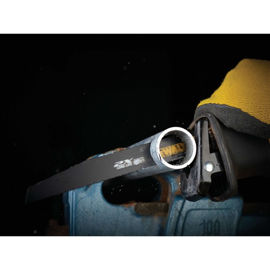 DEWALT saw blade cutting a metal pipe held in a blue vise, with a yellow-gloved hand operating the tool.