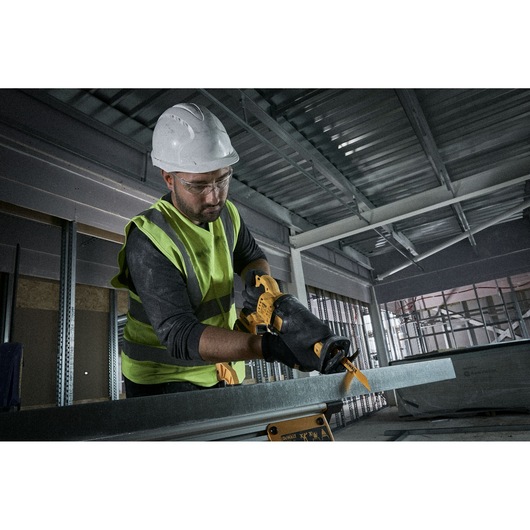 Worker using a yellow DEWALT saw to cut metal in an industrial setting, wearing safety gear and gloves.