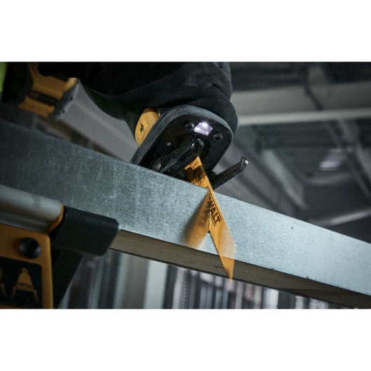 DEWALT saw blade cutting through metal, held by a gloved hand in an industrial setting.