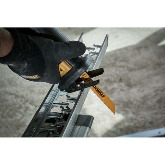 DEWALT saw blade cutting through metal, held by a gloved hand during a work process.