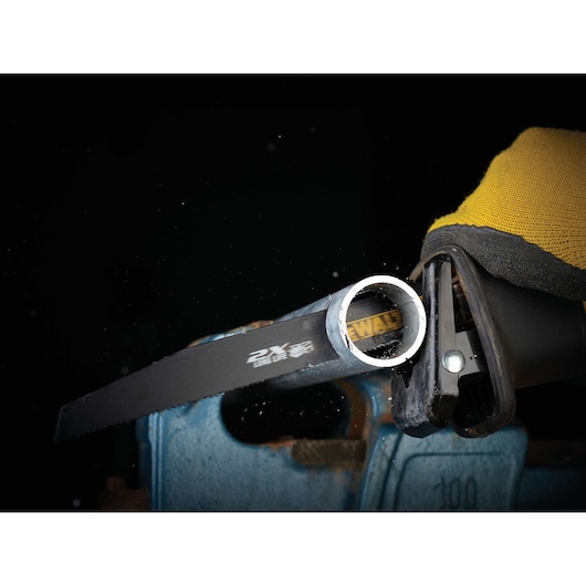 DEWALT saw blade cuts through a metal pipe. Worker wears yellow gloves for safety.
