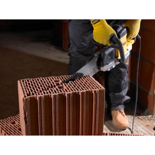 Person uses DEWALT electric saw to cut a large hollow brick block on a construction site.