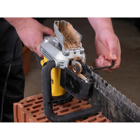 Person uses a hex key to adjust or maintain a DEWALT saw on a brick surface.