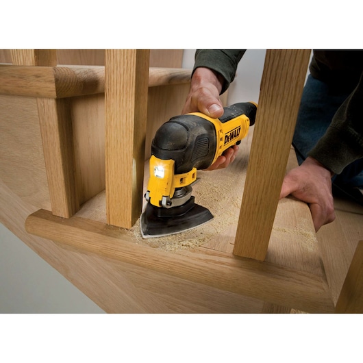 DEWALT DT3093 sander in use, sanding wood near stair rails. Fine dust is visible on the wooden surface.