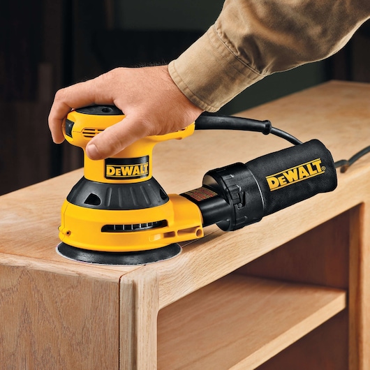 DEWALT sander being used on wood furniture corner.