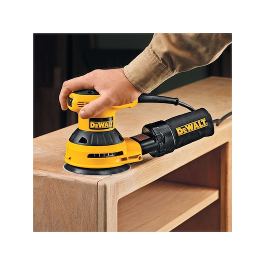 A DEWALT sander is used to smooth a wooden cabinet surface.