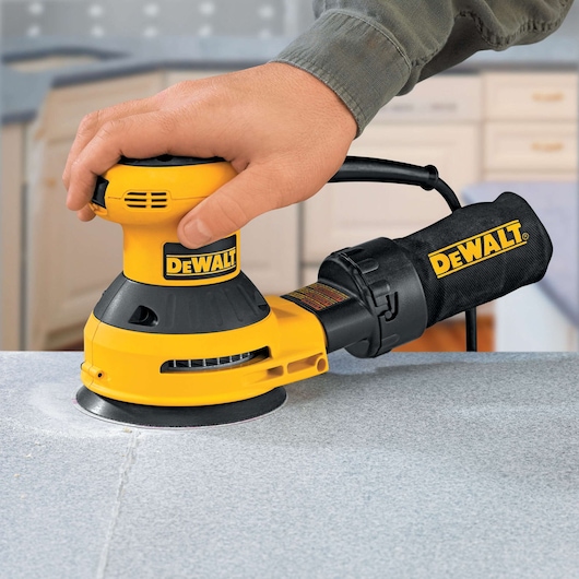 DEWALT handheld sander is being used to smooth a countertop surface in a home setting.