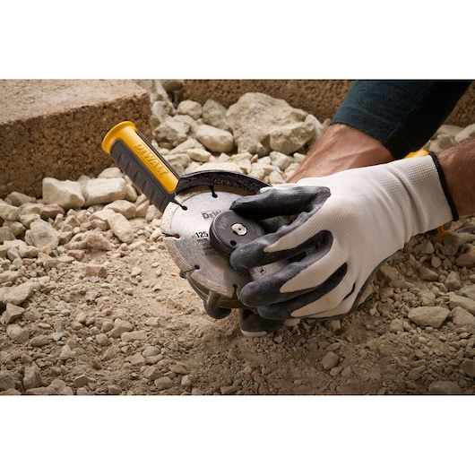 Gloved hands using a DEWALT DT3559 cutting tool on rocky ground.