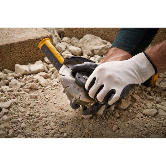 Gloved hands adjusting a DEWALT angle grinder on rocky ground, suitable for construction or masonry work.