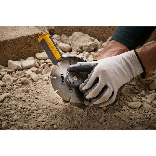 Gloved hand using DEWALT DT3559 angle grinder on rocky ground during cutting or construction.