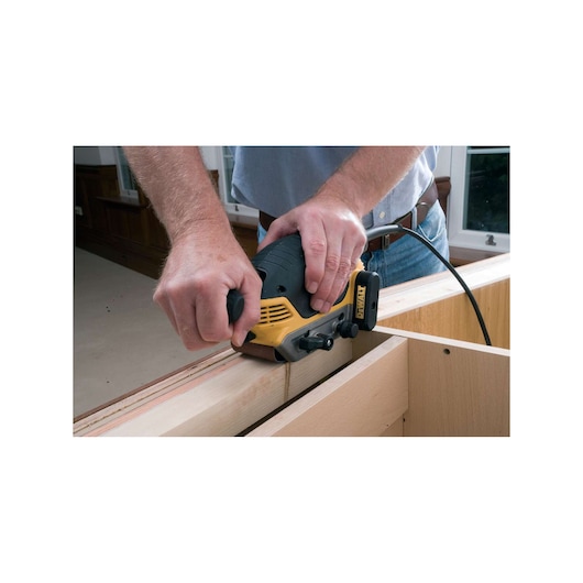 Person using a DEWALT electric planer to smooth wooden boards indoors.
